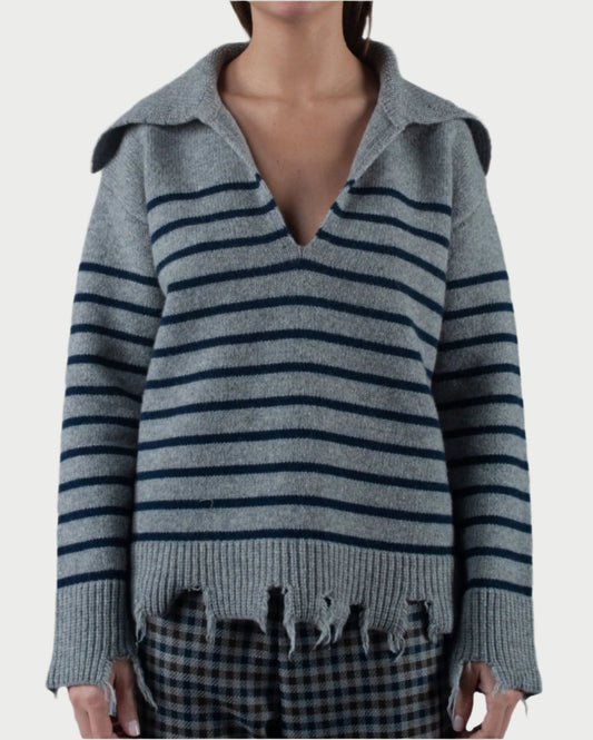 A person is wearing the Mariniere Sweater by Phisique du Role, a gray oversized wool blend piece adorned with dark horizontal stripes and featuring a wide V-neck collar. The distressed hem adds character to this stylish sweater. Paired with plaid pants, the ensemble stands out against the off-white background.