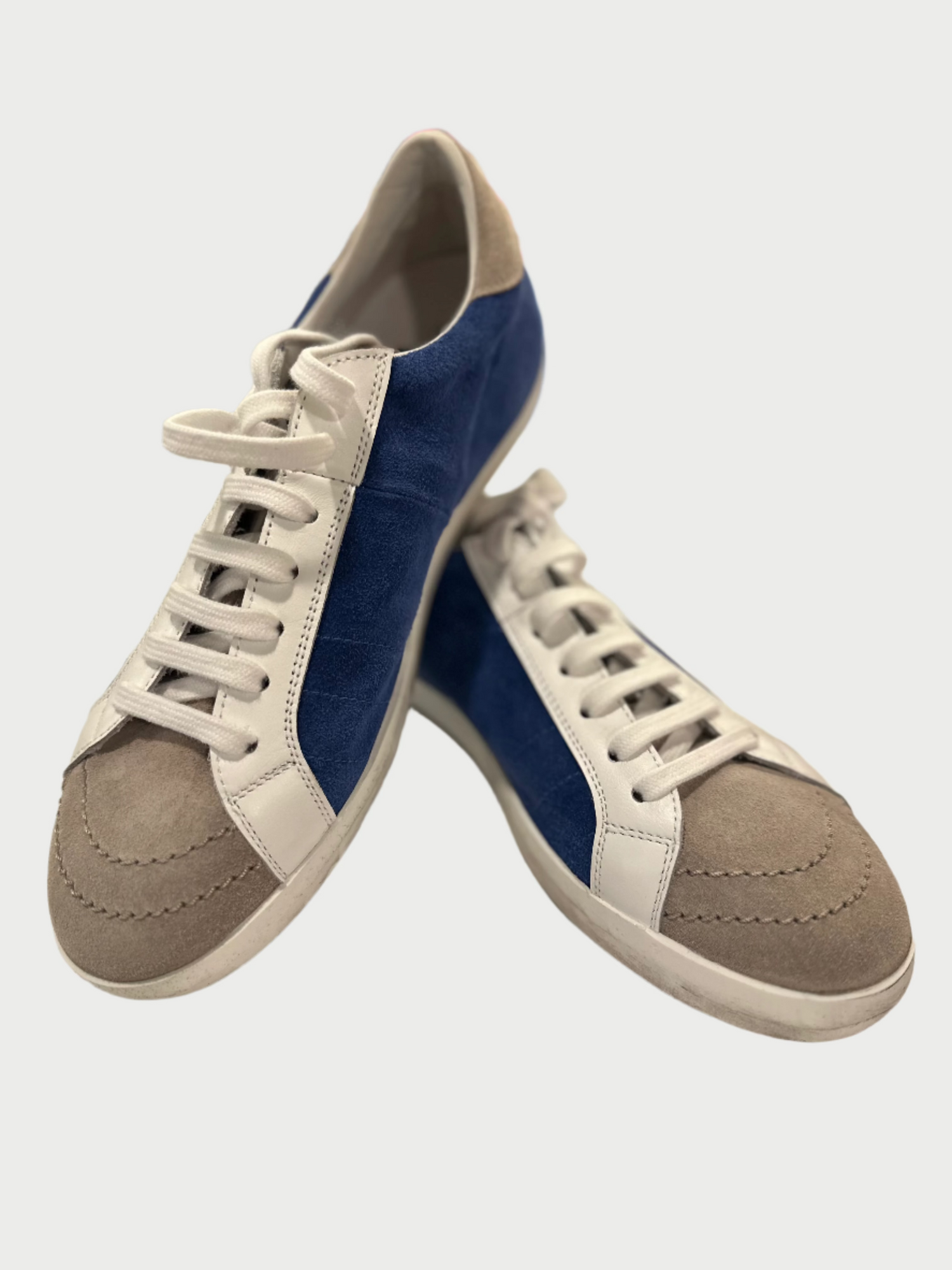 The Blue Sneakers by Primabase combine style and functionality, featuring blue sides, beige suede toe caps, and striking white leather accents. These fashionable sneakers are complemented by crisp white laces set against a plain white background.