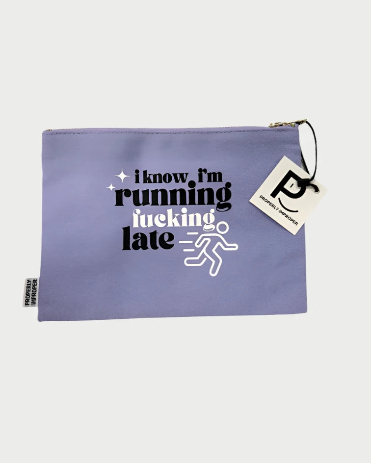 This sassy gift from Properly Improper, the Improper Pouches, features a bold purple design with black and white text stating, "I know I'm running fucking late," alongside a white runner icon. The pouch showcases a logo tag attached to the zipper and adds flair with unexpected gold satin accents for extra durability.