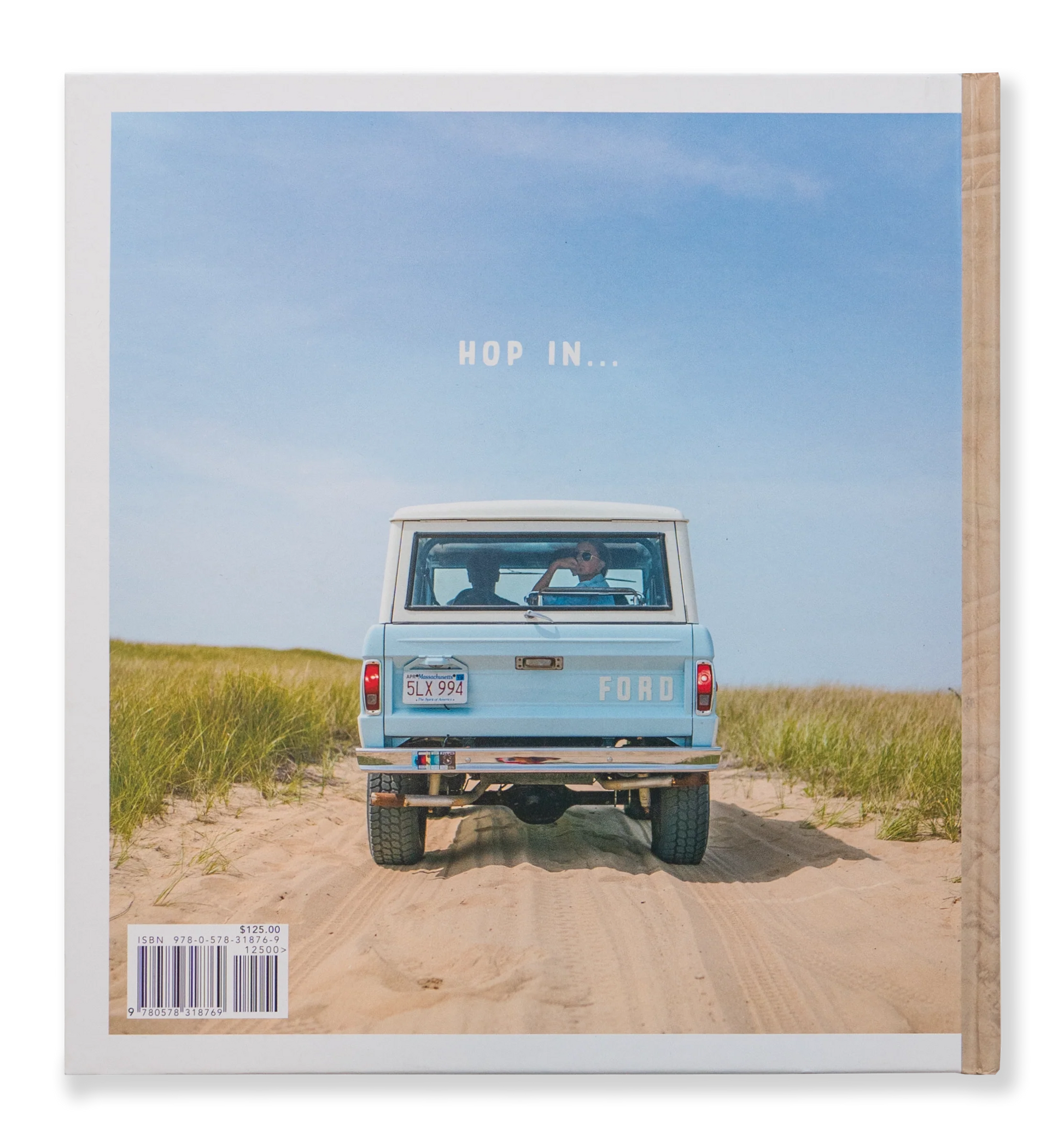 A vintage blue Ford truck cruises along a sandy path through grassy dunes beneath a clear blue sky. A person is visible through the rear window, reminiscent of scenes from Johnny Vacay's Beach Rides Book. Above the truck, the text reads: "HOP IN...".