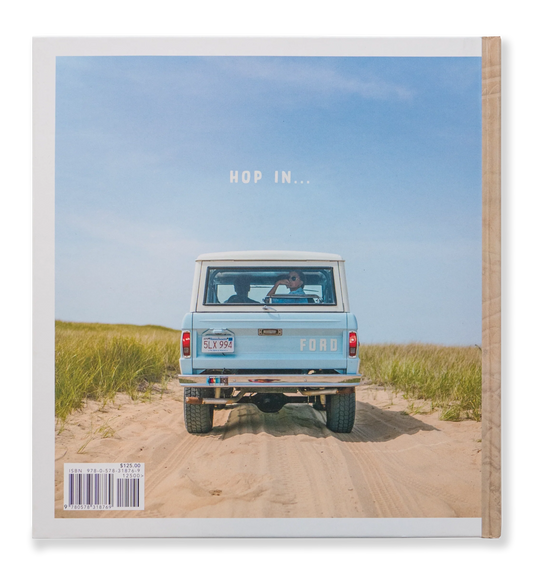 A vintage blue Ford truck cruises along a sandy path through grassy dunes beneath a clear blue sky. A person is visible through the rear window, reminiscent of scenes from Johnny Vacay's Beach Rides Book. Above the truck, the text reads: "HOP IN...".