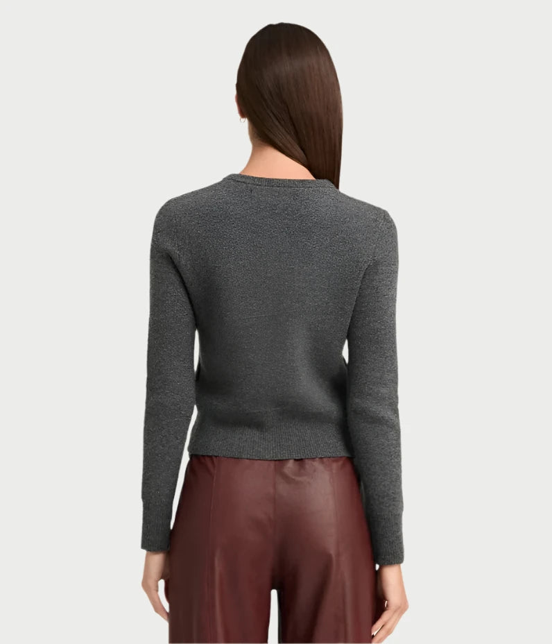 A person with long hair stands facing away, wrapped in the ultra-soft Baby Cardigan in Charcoal by SPRWMN, paired with brown leather pants. The background is a plain light gray, evoking the cozy allure of Mongolian Cashmere.