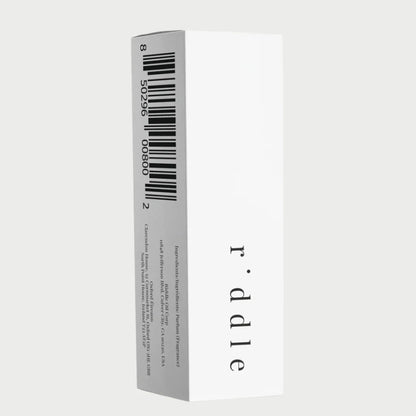 A tall, rectangular white box features the brand name "Riddle Oil" in lowercase letters on the side, highlighting a Santal fragrance infused with sandalwood undertones. One face of the box displays a large barcode, while delicate product information is printed in small text along another side.