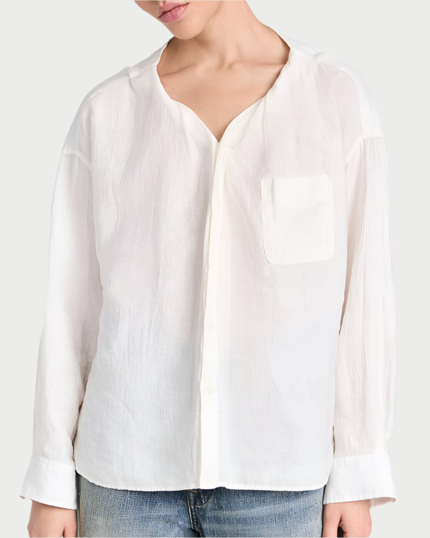 A person is wearing R13's Twisted Neck Shirt, a loose-fitting white button-up with a chest pocket made from Japanese crinkle lyocell fabric, paired with blue jeans. The image focuses on their upper body against a light, neutral background.