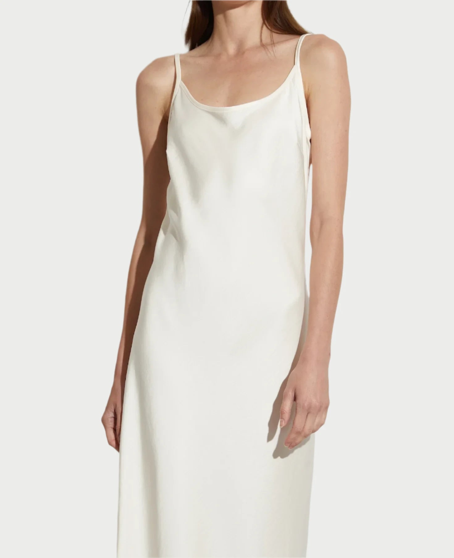 A person wearing the elegant Ivory Haley Slip Dress by Saint Art NY stands against a plain white background. The heavyweight charmeuse satin dress features thin straps and has a simple yet graceful appearance with a relaxed fit. The person's right arm hangs naturally by their side, and their face is not visible.