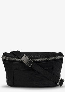 A black lamb skin leather Belt Bag with a textured surface, featuring gunmetal hardware, including a silver zipper on the front and a buckle on the adjustable strap. The compact and stylish Status Anxiety cross body bag has two small pockets on the front.