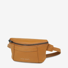 Load image into Gallery viewer, A tan leather Belt Bag with a pebbled texture and visible gunmetal hardware on the front zipper pocket and top main zipper closure. The adjustable strap, made of matching lambskin leather, allows it to be worn as a cross body bag. &quot;Status Anxiety&quot; is embossed on the front.