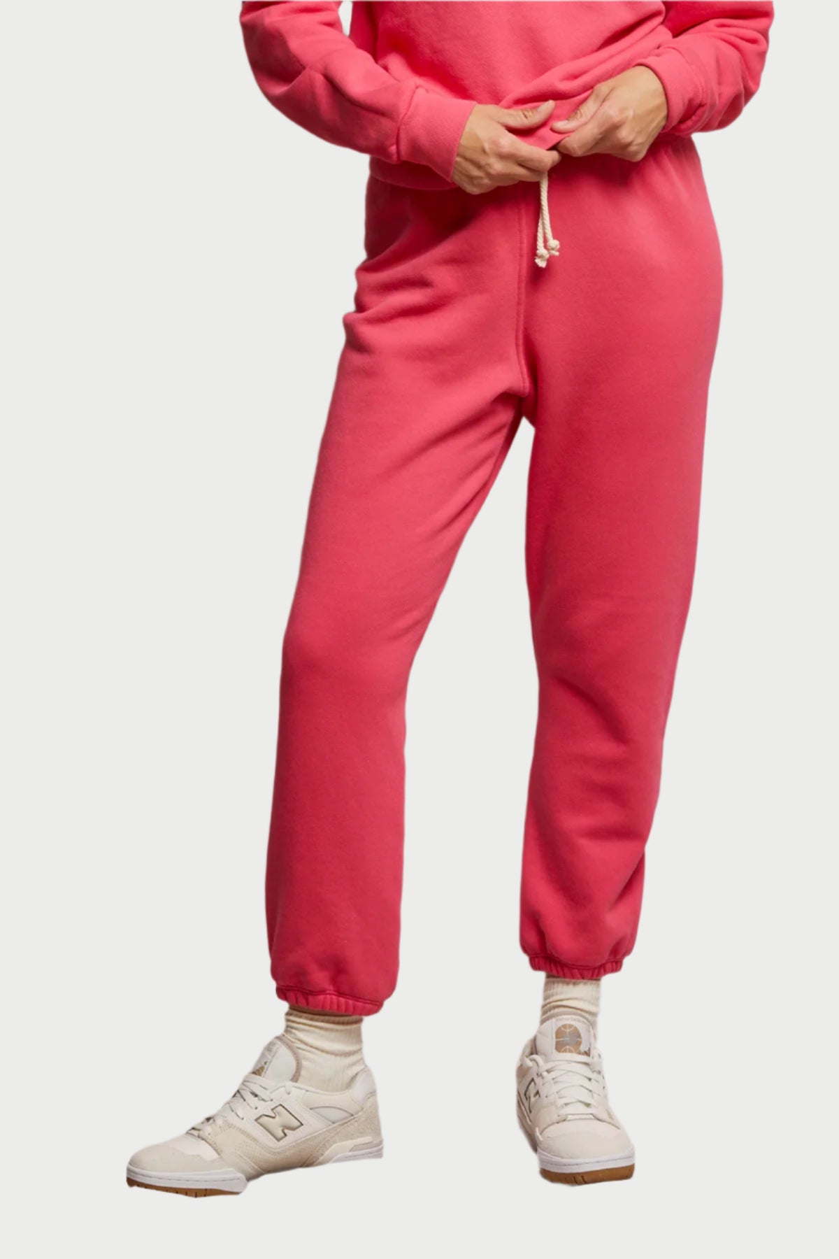 Dressed in perfectwhitetee's Stevie Sweatpant, a cozy red jogger made from soft cotton fleece with an adjustable drawstring, they pair it with matching sweatshirt, white sneakers, and socks against a light-colored background.