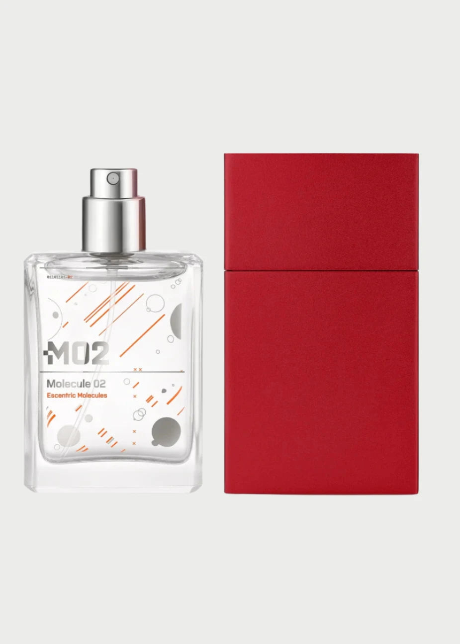 A clear glass bottle of Escentric Molecules 02 Travel size perfume with a minimalist design, featuring an orange geometric pattern. The bottle is positioned next to its sleek red rectangular box on a white background. Known for portable fragrances, Escentric Molecules boasts a silver spray nozzle on top, fitting seamlessly into any minimalist case.