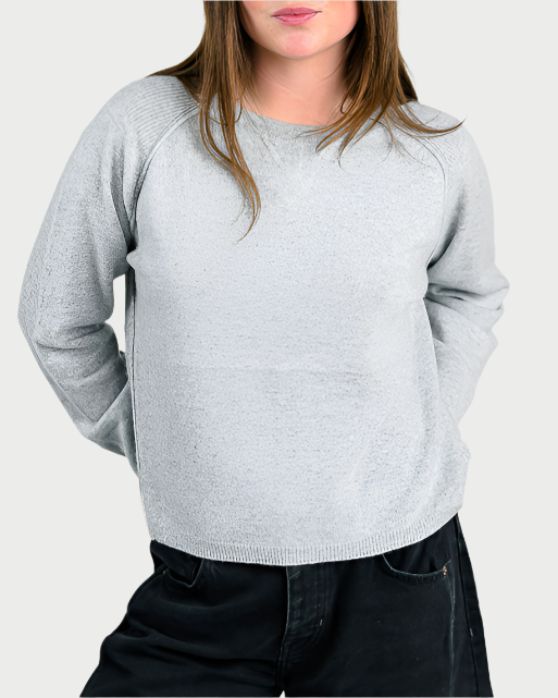 A person in an Archer Athletic Cashmere Sweater with long sleeves and dark pants stands against a plain background, hands behind their back. Their long brown hair partially covers their face, making this outfit an everyday essential.