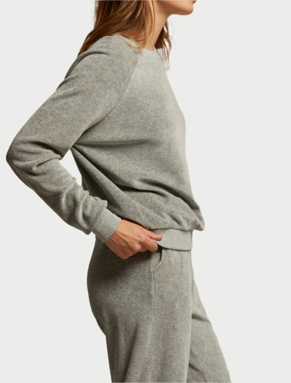 A person in a relaxed pose is wearing the Stella Velour Sweatshirt by perfectwhitetee, along with matching sweatpants, hands in pockets against a plain backdrop, effortlessly combining style and comfort.