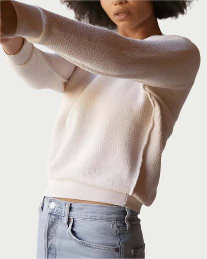 A person wearing the Ziggy Sweatshirt by perfectwhitetee, featuring a classic cream color with exposed seam detailing, paired with light blue jeans. The individual has curly hair and is extending their arms forward against a plain and neutral background.