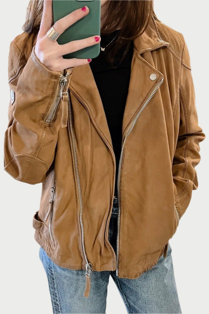 A person with long hair is taking a mirror selfie wearing a Mauritius Nubuck Jacket over a black shirt and R13 jeans. They hold their phone, which has a green case, with one hand, while their other hand is in their jacket pocket.