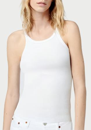 A person with shoulder-length blond hair is wearing a white RE/DONE Ribbed Tank and matching white pants. They are standing against a plain light gray background, looking slightly to the side with a neutral expression.