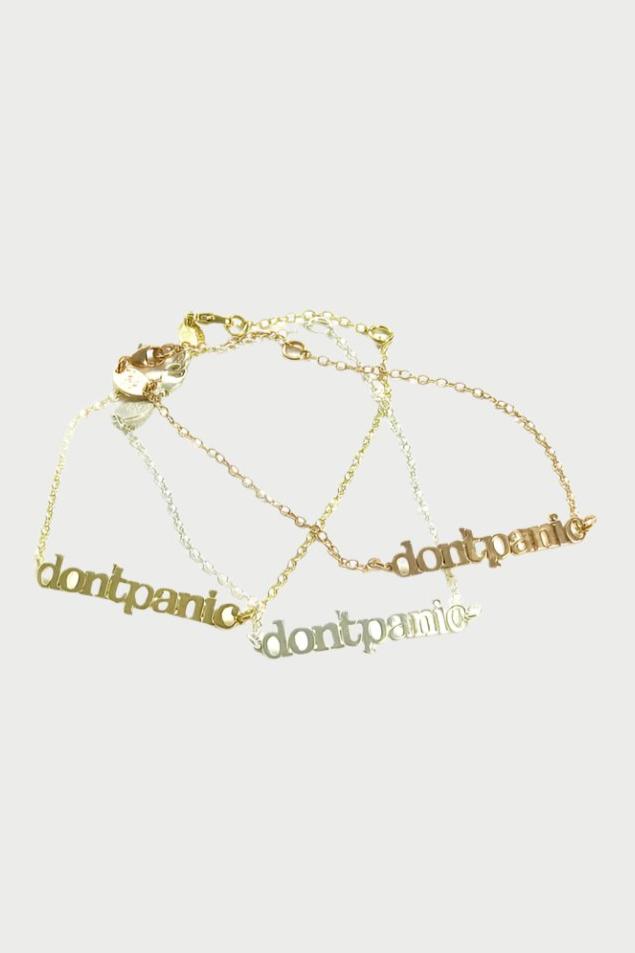 Three Simply Eartha "Don't Panic Chain Bracelet" feature chains of different finishes: one 14k gold plated, one sterling silver plated, and one in a darker metal. Each bracelet is laid out in a casual arrangement against a white background.