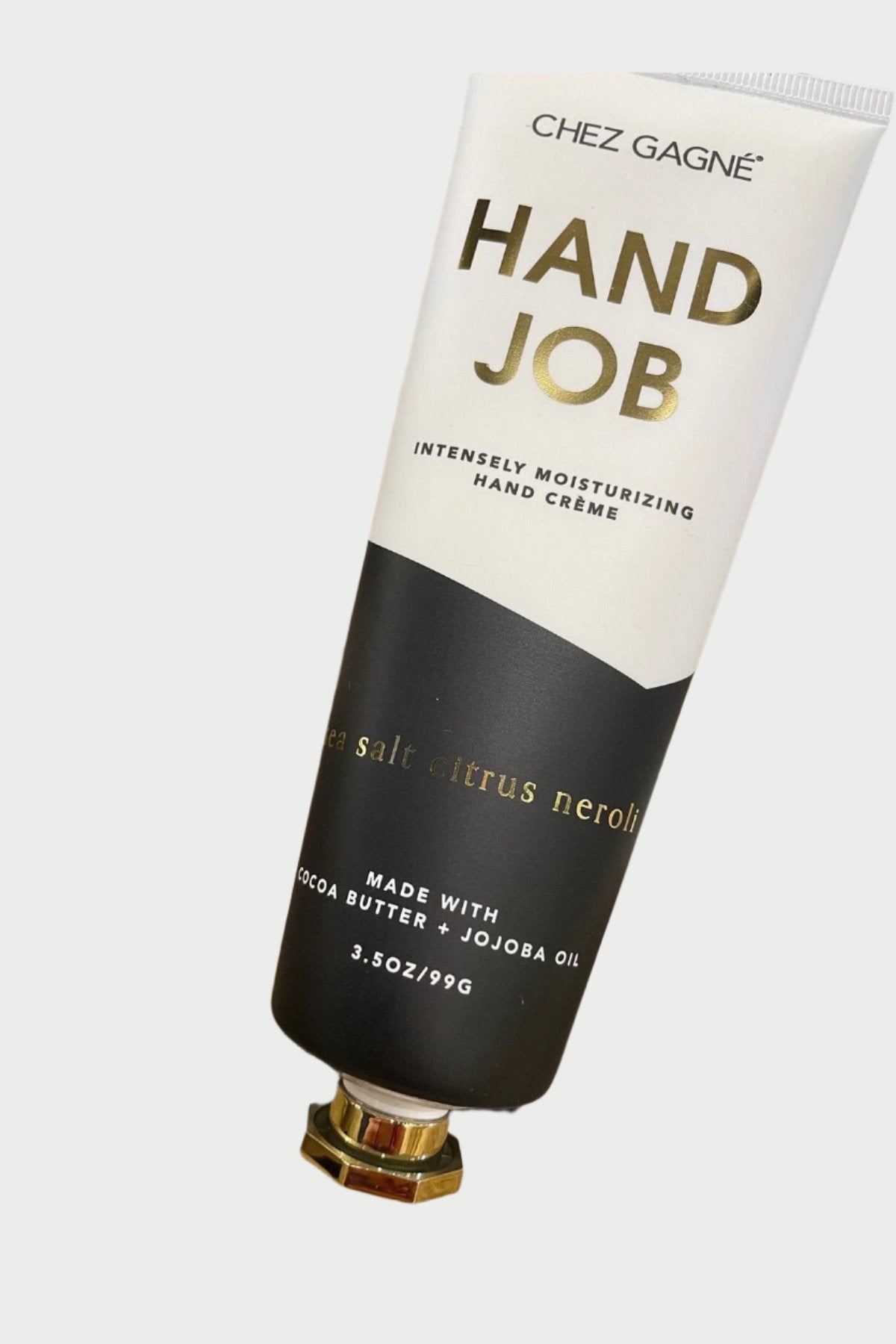 A tube of Chez Gagné Hand Creme intensely moisturizing hand crème with sea salt and citrus neroli scent, placed on a beige fuzzy surface. The packaging highlights that it is made with cocoa butter and jojoba oil, and weighs 3.5 oz (99 grams).