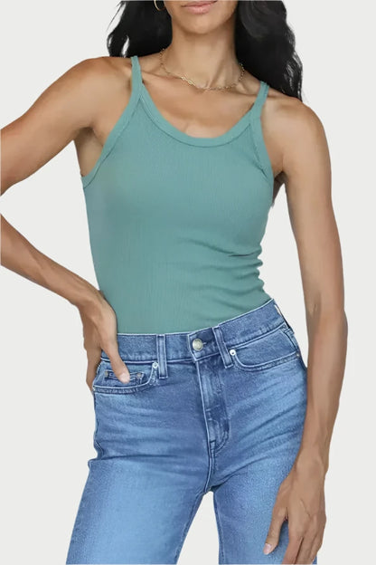 A person with long, wavy dark hair is wearing a green, form-fitting ribbed Annie Tank from perfectwhitetee and blue jeans. They are posing confidently with one hand on their hip against a plain background.