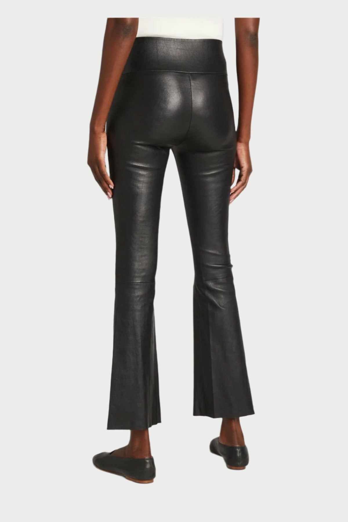 An individual dressed in SPRWMN's Leather Crop Flare Pants and black shoes poses against a simple, light backdrop. The chic, snug pants exhibit a delicate crop flare at the hem, with only the rear view of the legs on display.